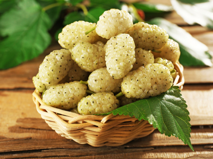 A basket of fresh white mulberries with leaves on a wooden table