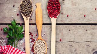 Wooden spoons of green, white, and red peppercorns on a wooden table