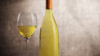 A bottle and glass of white wine against a dark background