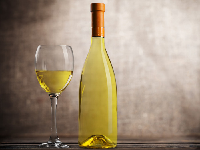 A bottle and glass of white wine against a dark background