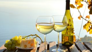 Wine glasses and a half-filled bottle of white wine with a plate of cheese slices and grapes on a wooden table