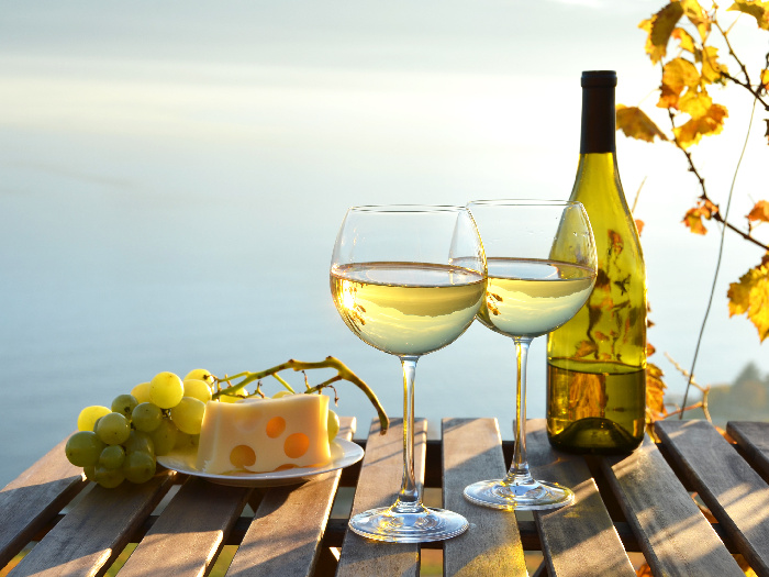 Two glasses of white wine, grapes, and cheese on a table outdoors