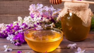 A jar and bowl of wildflower honey with fresh white and purple wildflowers on a wooden table