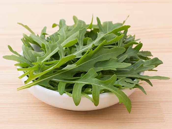 A bowl of fresh green wild lettuce leaves on a wooden table