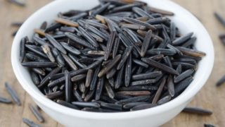 A white bowl of uncooked wild rice on a wooden table
