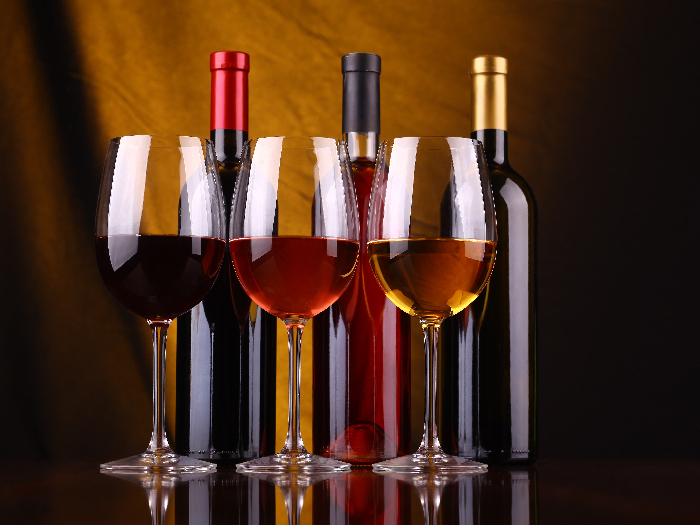 Three glasses of wine with three bottles stacked behind them