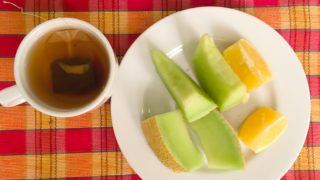 A cup of black tea made with a teabag, a plate of sliced winter melon and lime on a wooden table