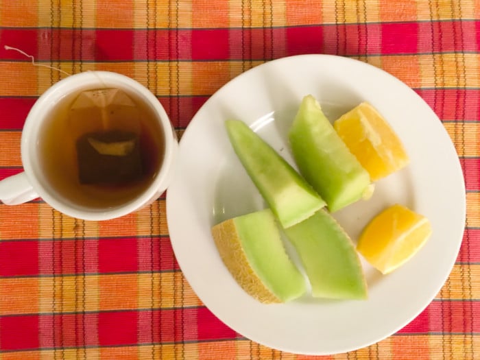 A cup of black tea made with a teabag, a plate of sliced winter melon and lime on a wooden table