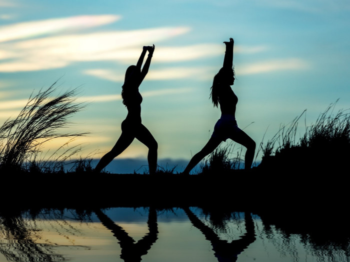 A picture of two women doing yoga around a water body