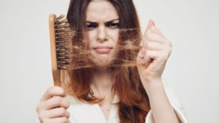 A girl upset with her hair loss standing with her comb that has many strands on a white background