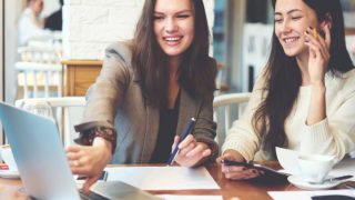 Two women smiling and working on laptops