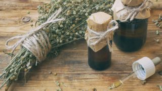 Bottles of wormwood oil and a bunch of dried wormwood herb on a wooden table