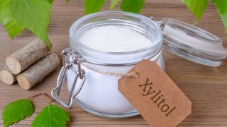 A jar of xylitol, a sugar substitute, with birch leaves and bark on a wooden table