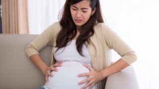 A pregnant Asian woman sitting on a couch suffering from yeast infection
