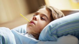 A young girl in bed suffering from yellow fever with a thermometer in her mouth