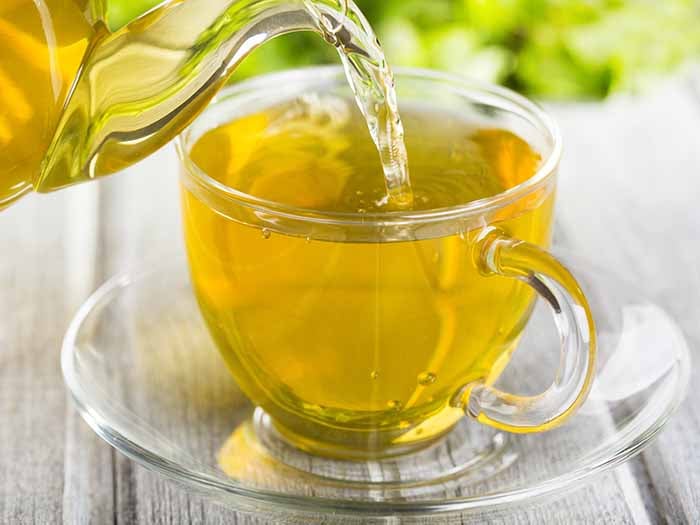 Pouring hot yellow tea from a teapot into a cup on a wooden table