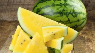 A whole watermelon and sliced yellow watermelon on a wooden table