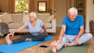 An old couple suffering from osteoporosis practicing yoga at home in the living room