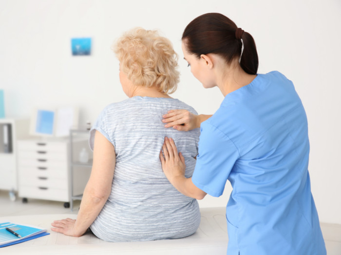 A nurse checking the spine of an older woman