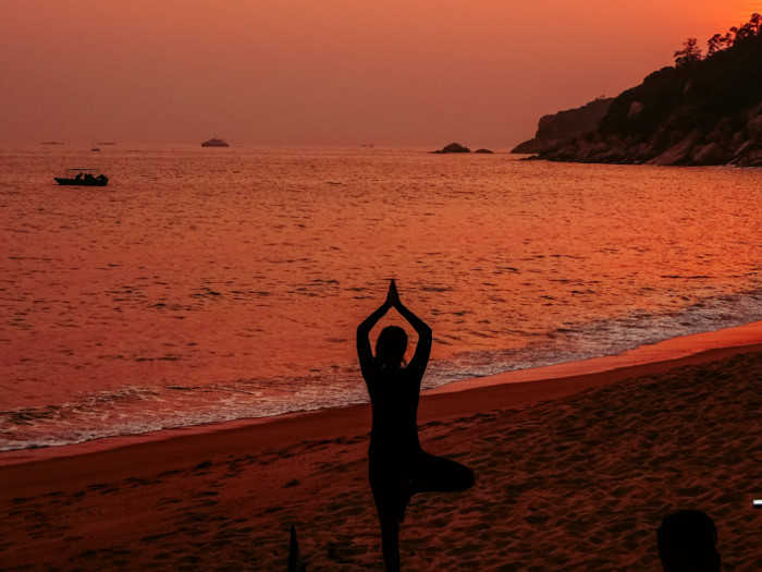 A silhouette of a person doing yoga on the beach at the time of sunset