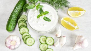 bowl of yogurt with cucumbers, dill, and lemon wedges