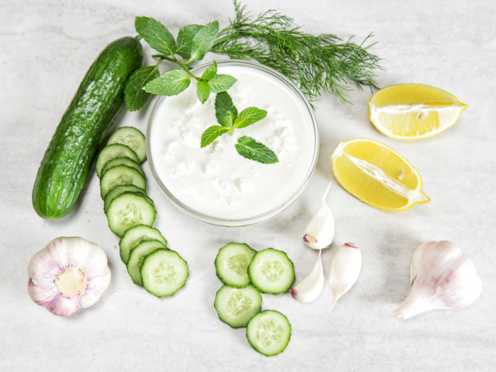 bowl of yogurt with cucumbers, dill, and lemon wedges