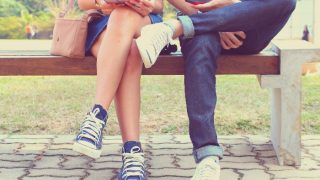 Close up of a young couple sitting on a bench, holding a tab and a smartphone