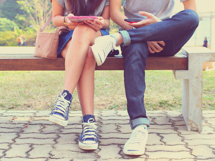 Close up of a young couple sitting on a bench, holding a tab and a smartphone