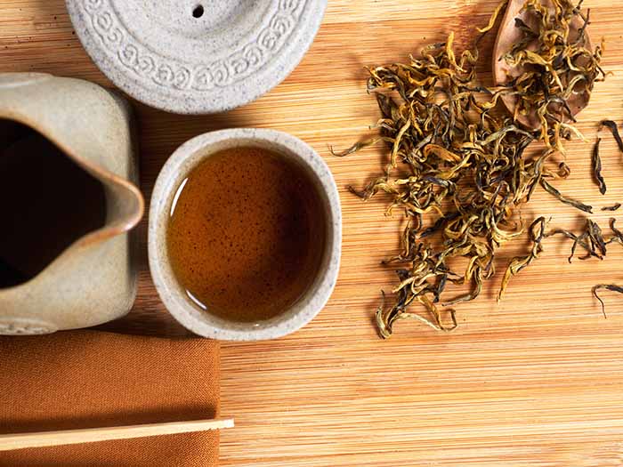 A jar and cup of Dainhong or Yunnan tea with a spoon of dried fresh Yunnan leaves on a wooden table