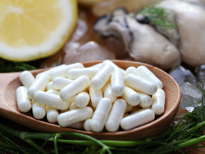 Zinc supplements on a wooden spoon with zinc-rich oysters and lime slices in the background