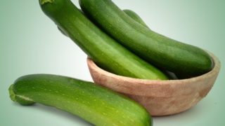 Close up shot of fresh green zucchini in a bowl against a light blue background