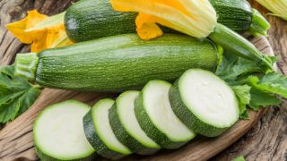 Whole and sliced dark green zucchini with zucchini squash blossoms on a wooden table